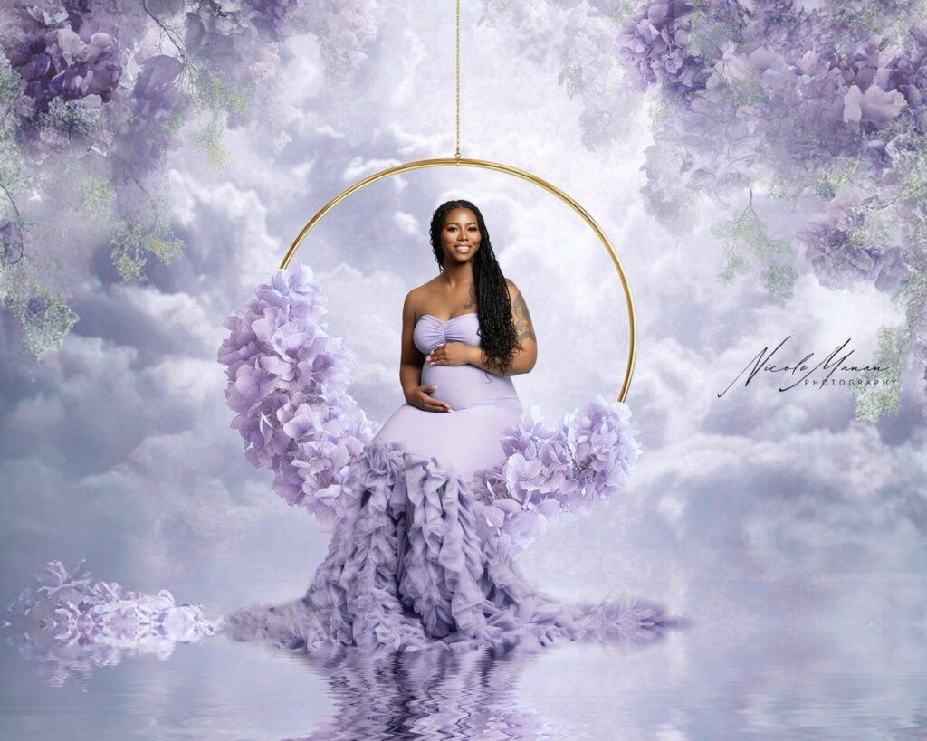 Elegant pregnant woman sitting on a floral moon swing in a dreamy, cloud-filled sky during maternity photoshoot.