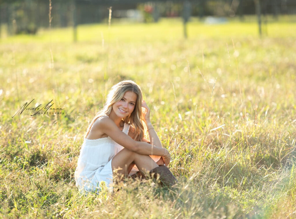 A girl having fun doing her senior session in Columbus, GA . She is sitting in a field.